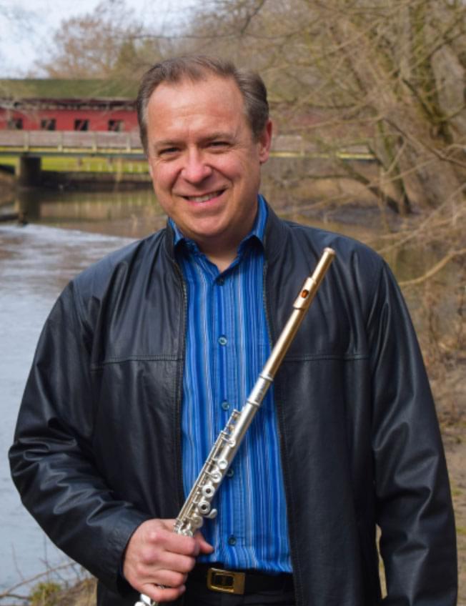 man stands out in the woods holding flute