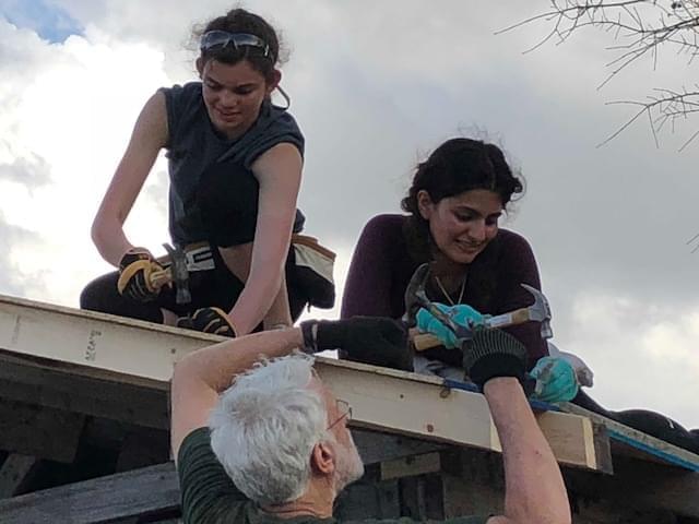 Students hammering shingles on the roof of a house