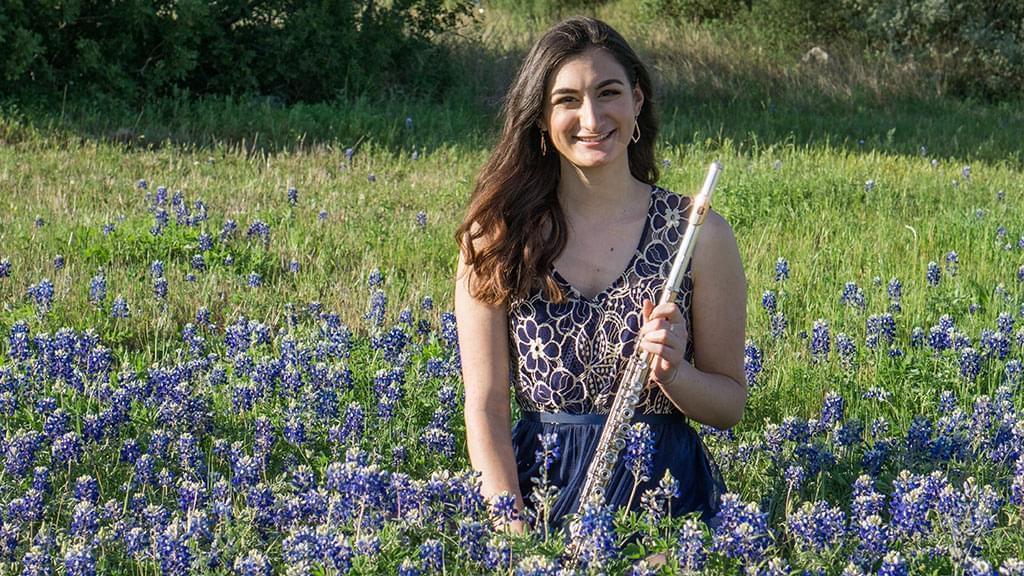 woman in blue dress sits with flute in field of flowers