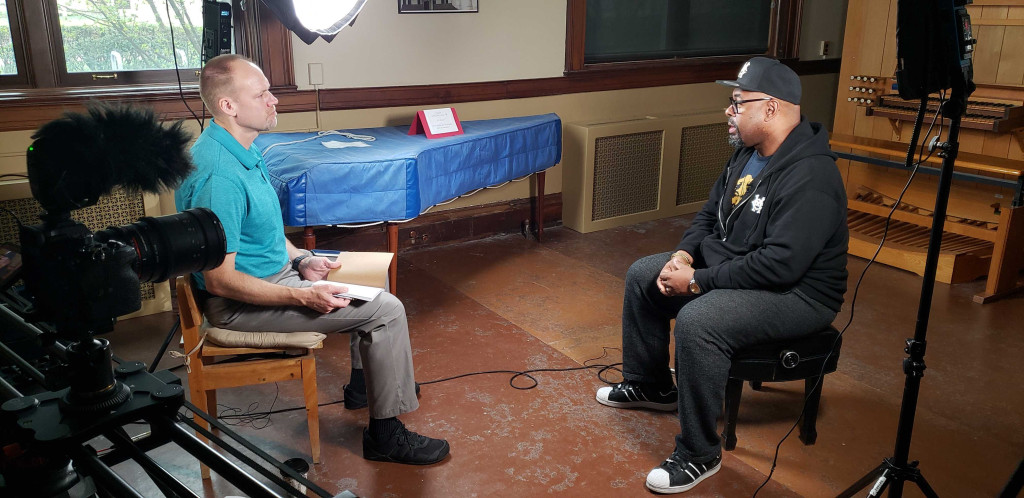 Two men sit down for an interview with cameras and lights