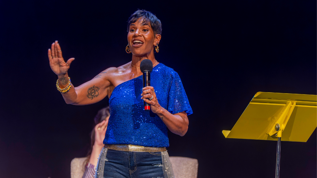 woman in blue top holding microphone speaks on stage