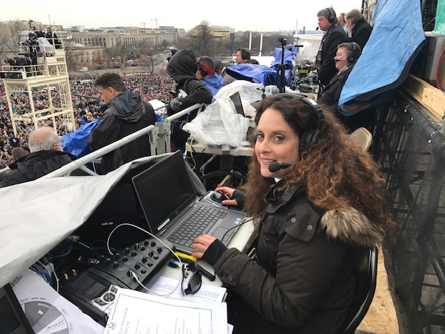 woman sits in stands with laptop and headphones