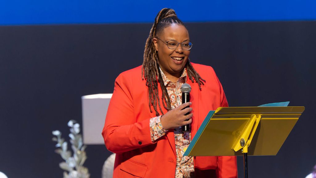 Women in orange blazer stands on stage with microphone