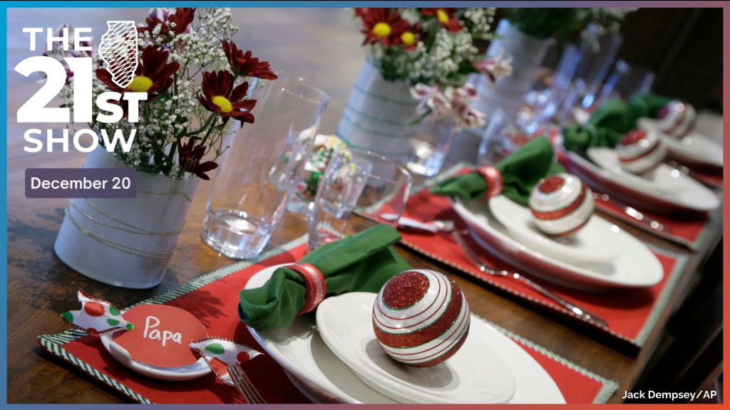 a brown wooden table set for Christmas with red placements, white plates, and green cloth napkins. There are small bouquets of flowers and Christmas ornaments at each setting