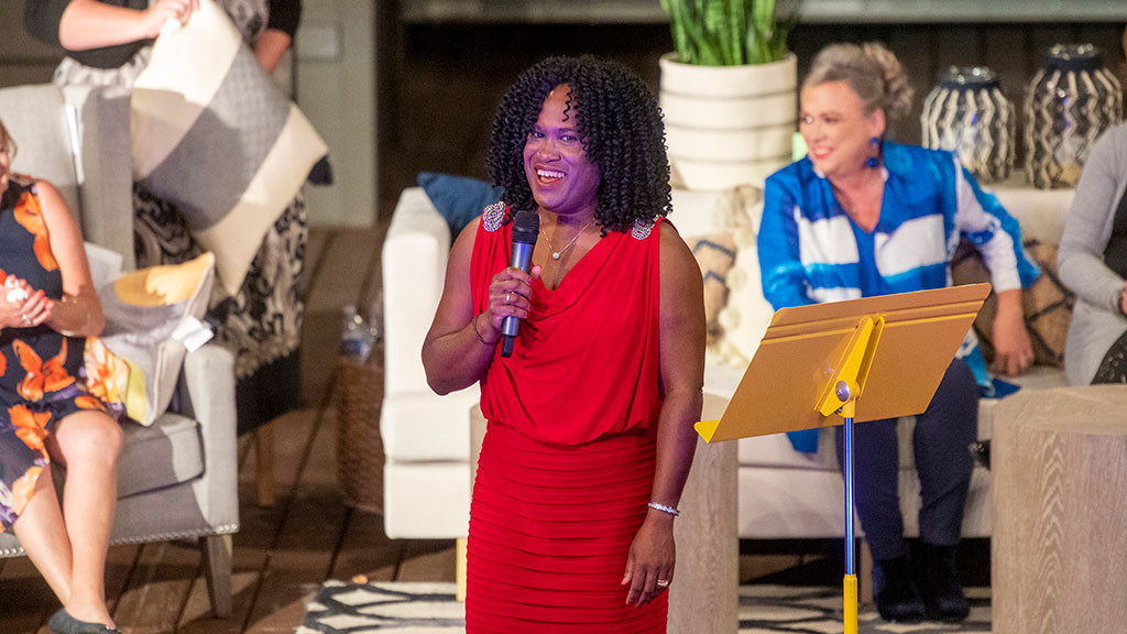 Woman in red dress on stage with microphone people sit behind her