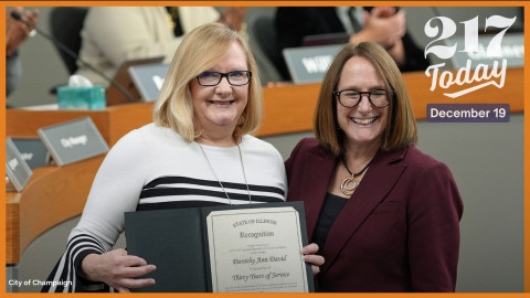 Dorothy David stands in front of members of city council applauding, holding a certificate of recognition.