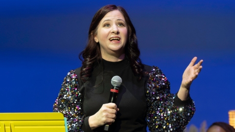 woman in black top holding microphone blue background