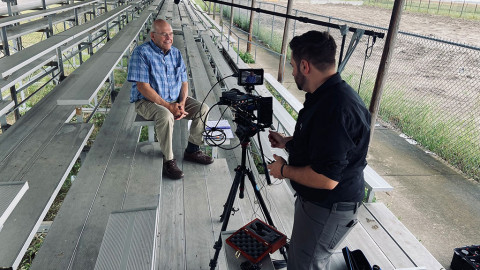 man interviews another man sitting on a bleacher