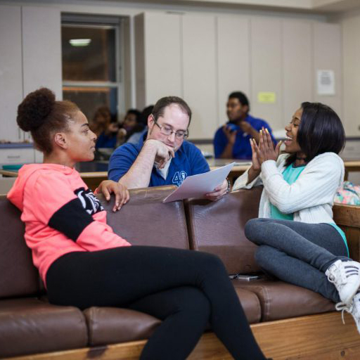 three people sit and talk over paperwork